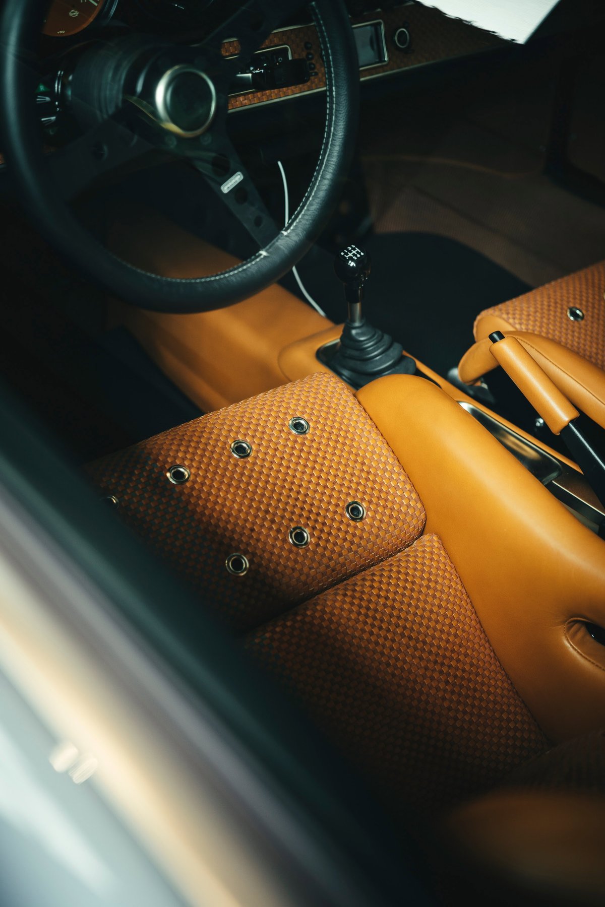 Classic Porsche 911 cockpit with tan leather trim, custom brown fabric seats & grommets, 5-speed manual shifter, and 3-spoke steering wheel.