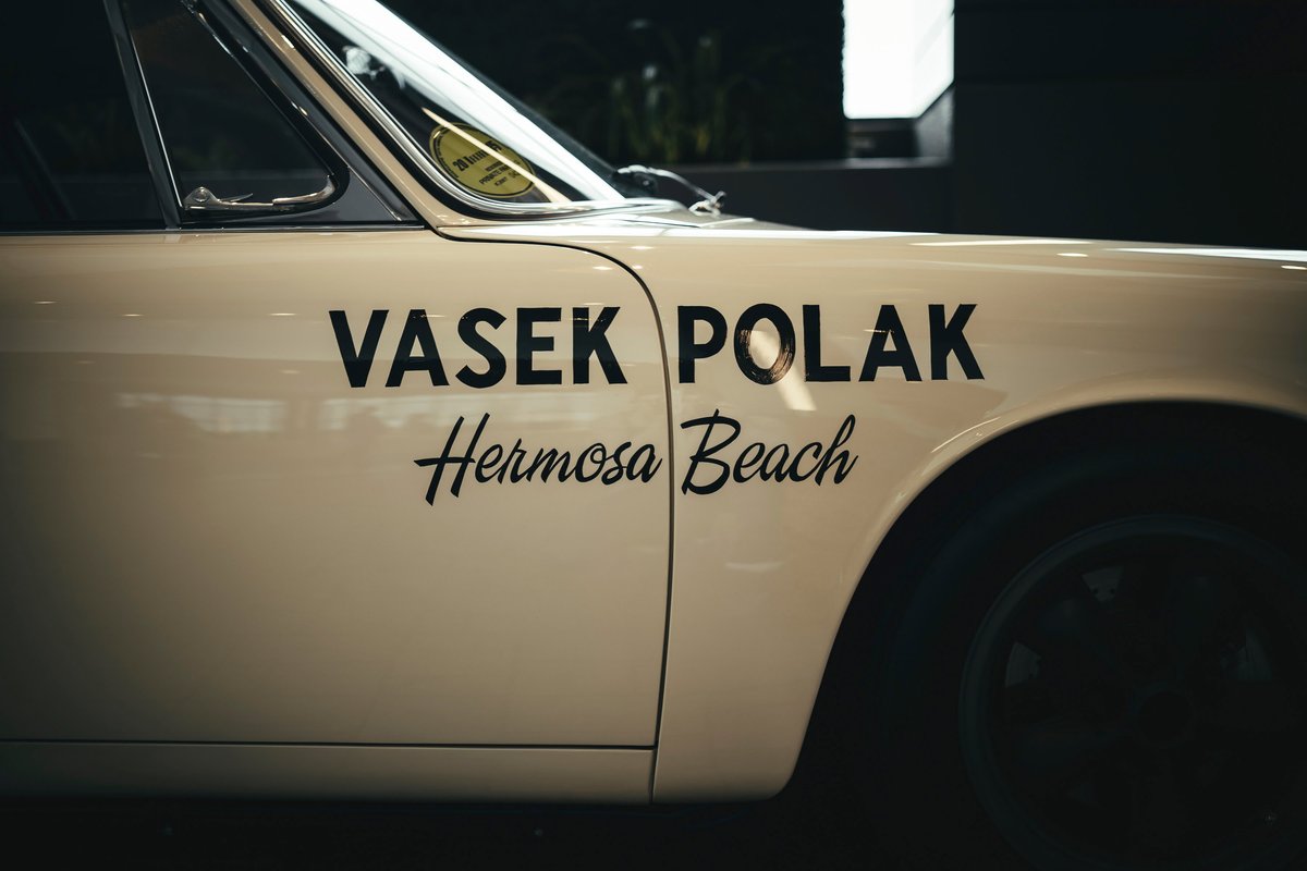 Off-white classic Porsche 911 front fender with iconic Vasek Polak Hermosa Beach livery, chrome trim, and dark Fuchs wheels.