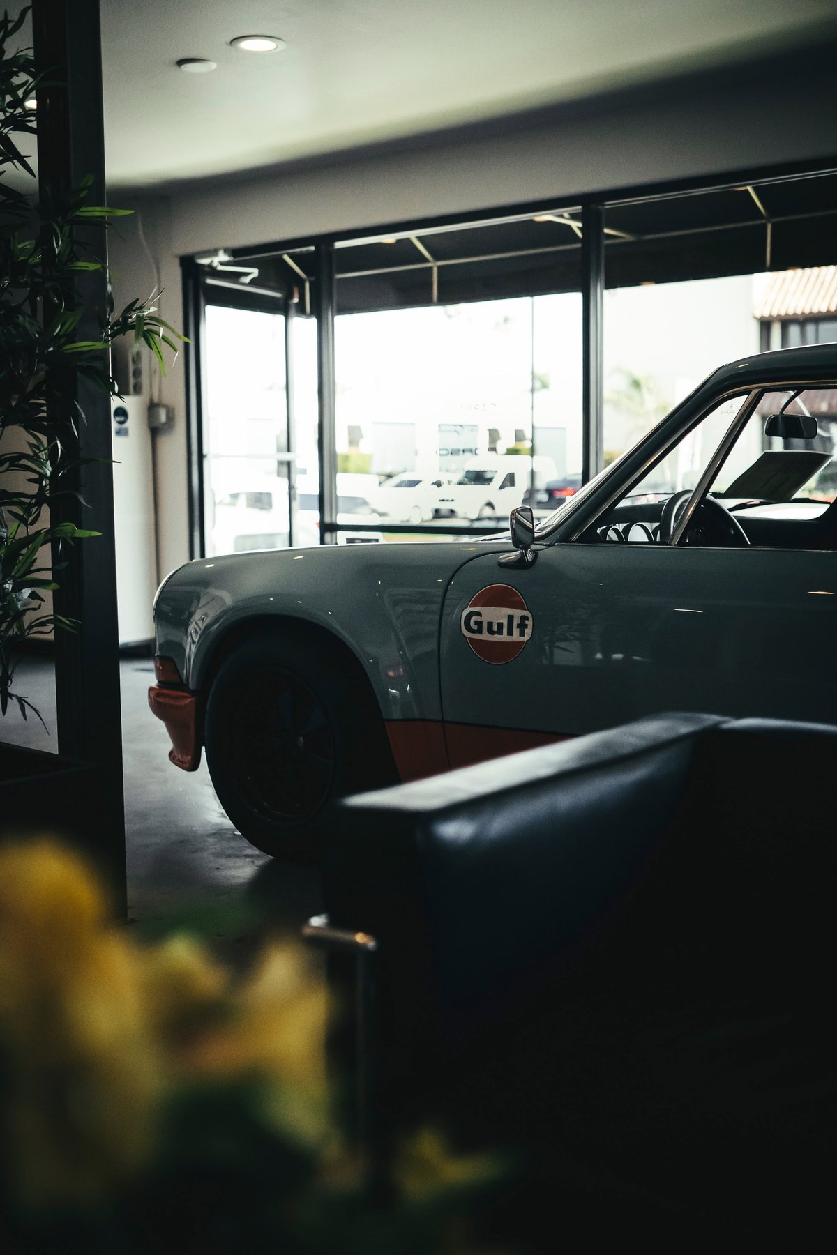 Front quarter view of a classic Porsche 911 in iconic Gulf livery: light blue with orange lower trim and a distinctive Gulf logo.