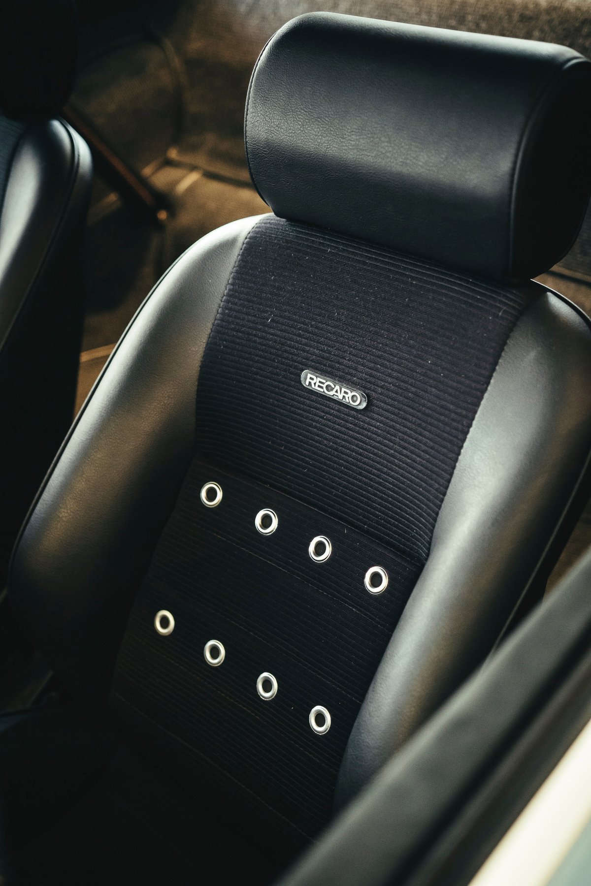 Close-up of a black Recaro sport seat with ribbed fabric and chrome grommets in a classic air-cooled Porsche interior.