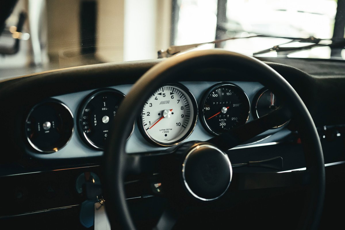 Classic Porsche 911 interior: black steering wheel, light blue dashboard, iconic five-dial instrument cluster with a central white tachometer.