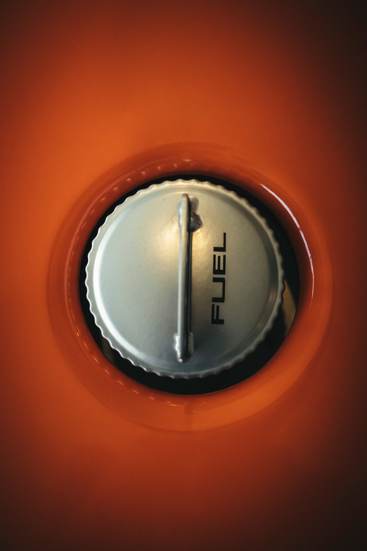 Orange vintage Porsche 911's exposed fuel filler cap. Brushed metal with "FUEL" text and classic lever.