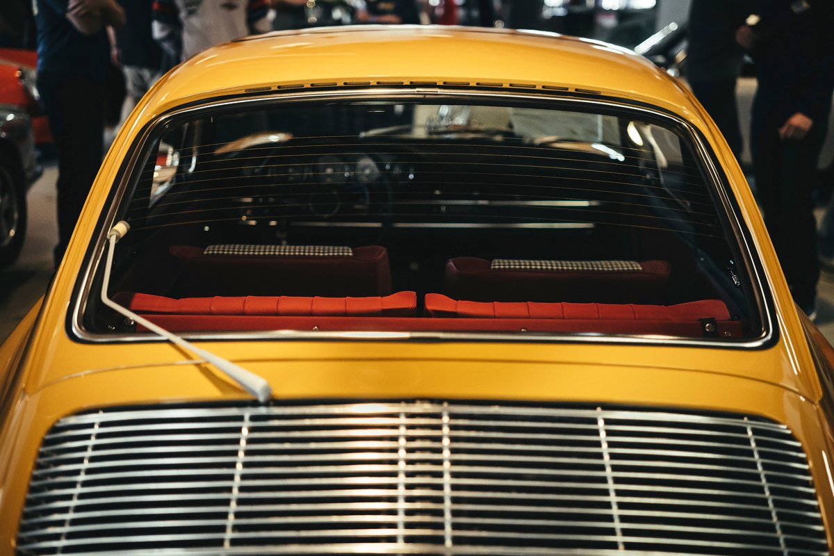 Vintage yellow Porsche 911 rear view showing chrome window trim, engine louvers, and red tartan interior.