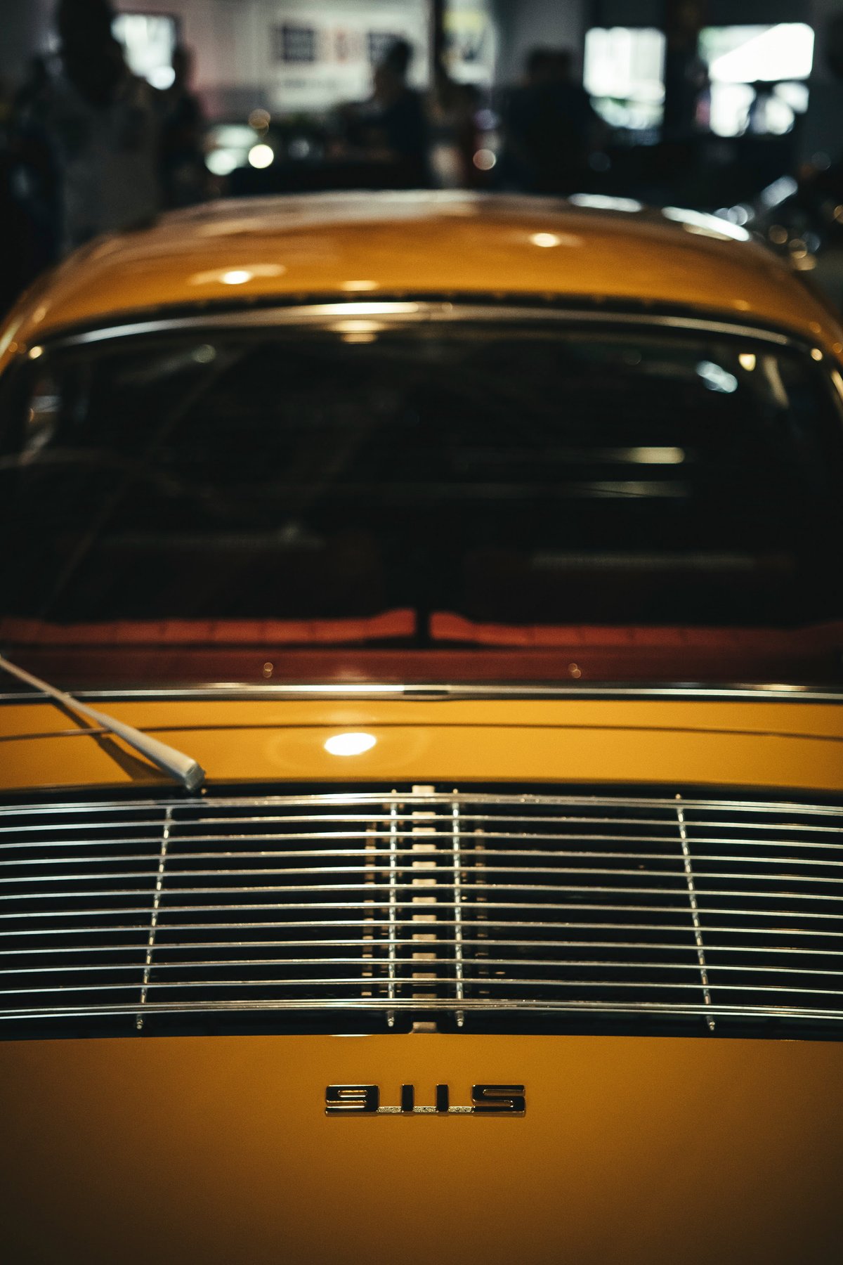 Close-up of a vibrant yellow classic Porsche 911S rear, highlighting its chrome engine grille and iconic "911S" badge.