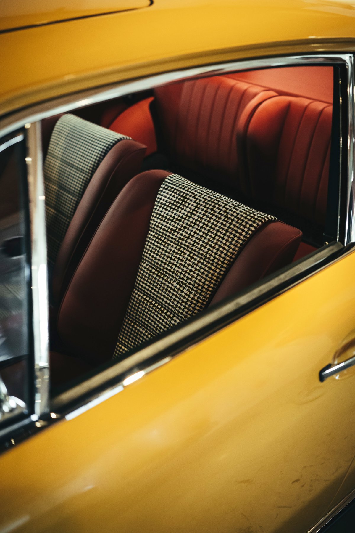 Yellow classic Porsche 911 interior. Rich brown leather seats with houndstooth fabric inserts and sleek chrome window trim.