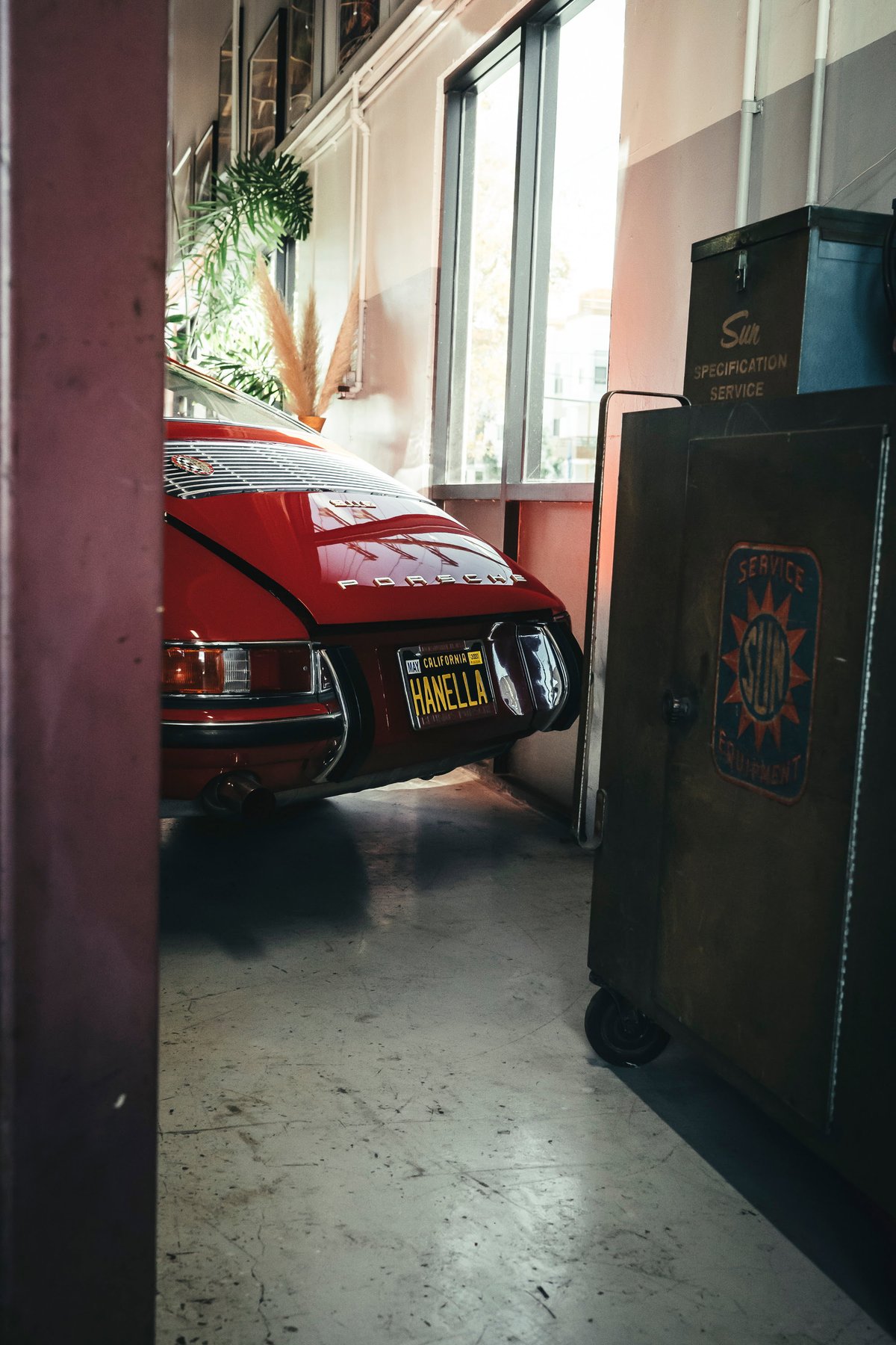 Vibrant red classic air-cooled Porsche 911 rear, featuring engine lid louvers, chrome bumperettes, and California plate.