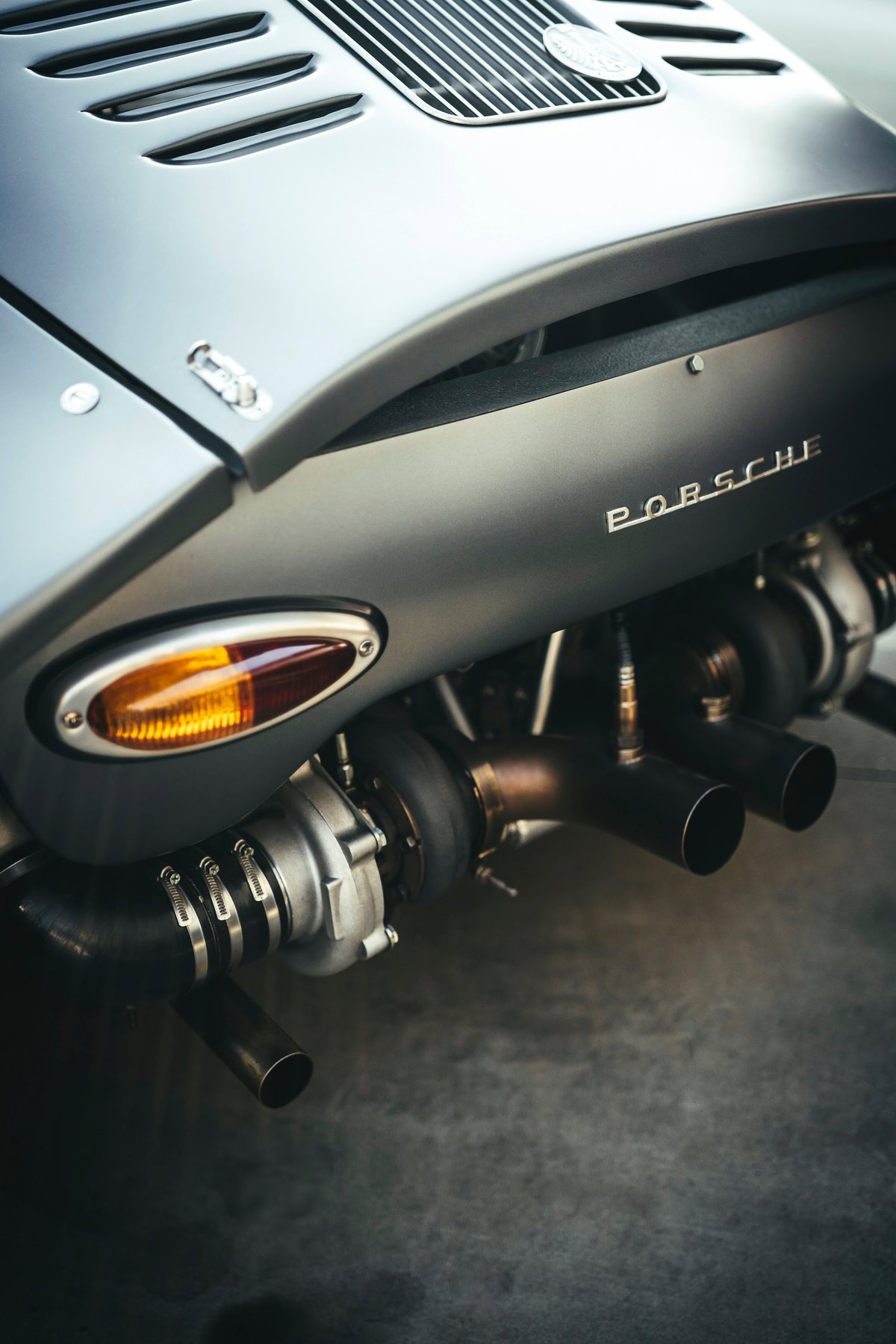 Custom matte dark grey Porsche 911 rear, featuring exposed twin turbos, bespoke exhaust tips, and classic amber taillight.