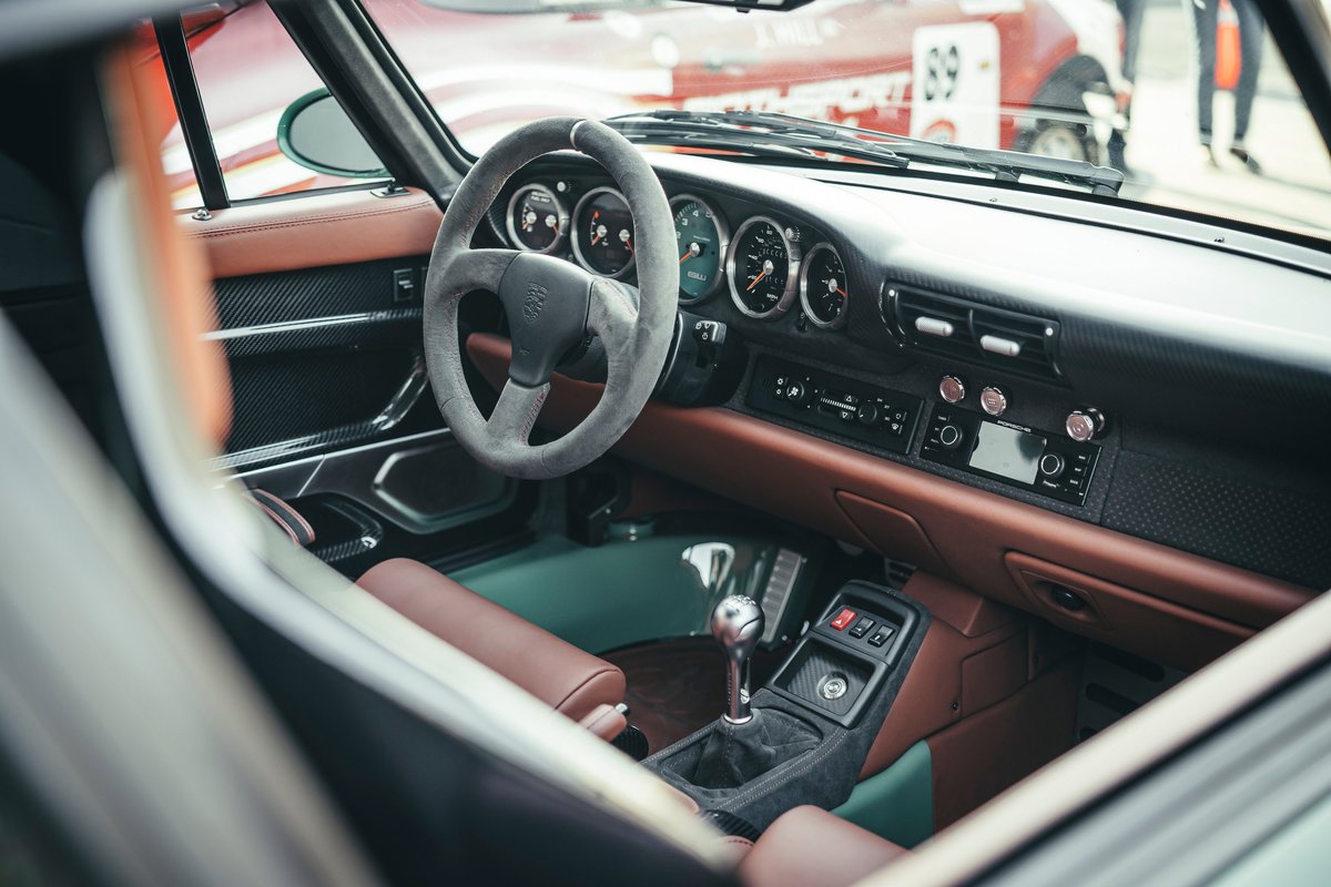 Porsche 964 interior: Alcantara wheel, brown leather dash trim, carbon fiber door cards, custom green carpet, manual shifter.