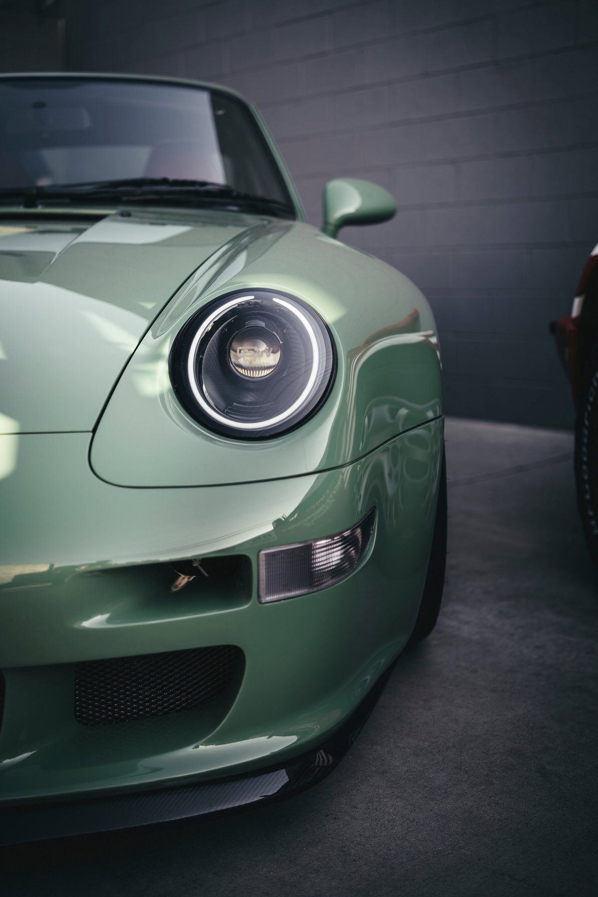 Front fender detail of a mint green Porsche 993 restomod, showcasing custom LED projector headlights & carbon fiber lip.