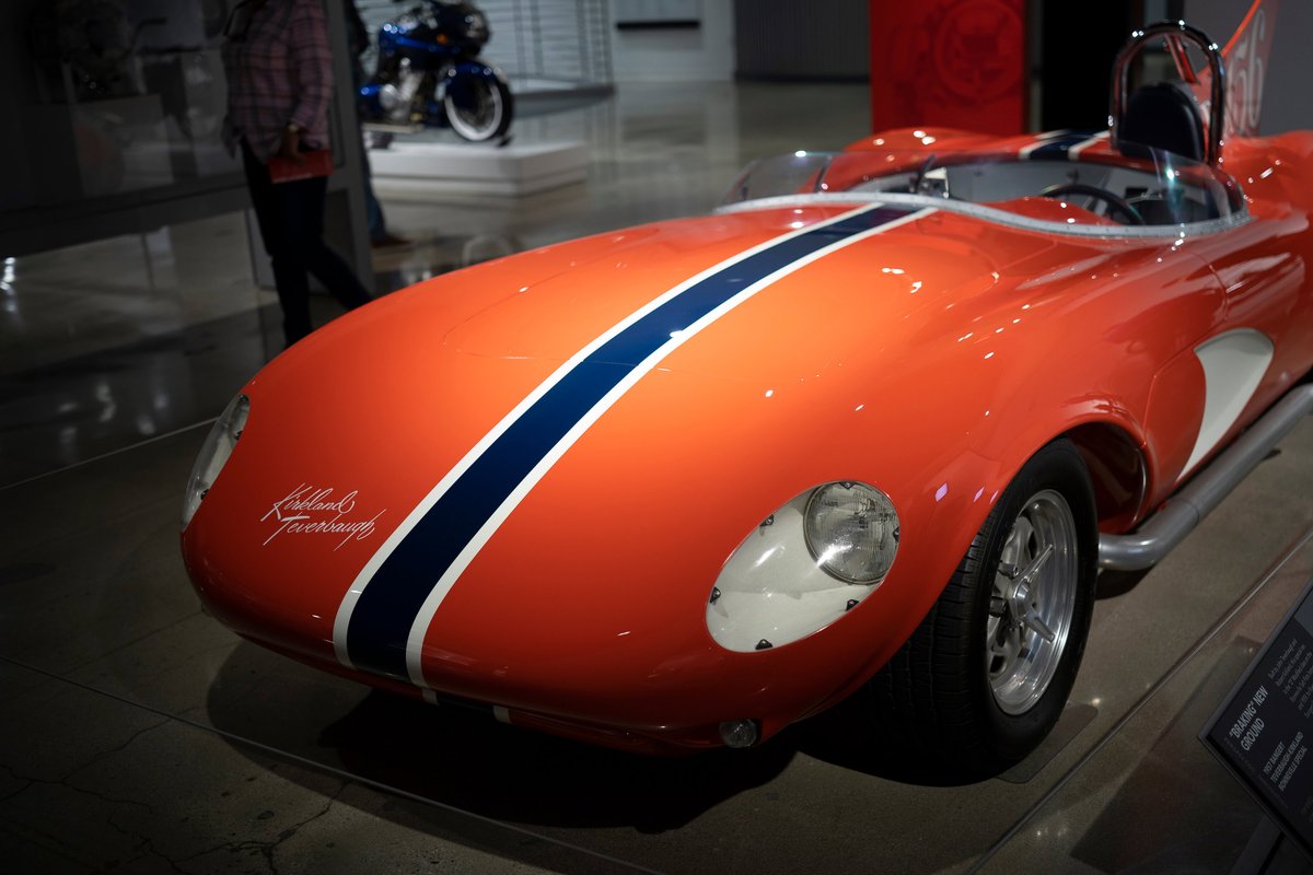 Front 3/4 view of an orange 1959 Corvette XP-87 Stingray Kjelland & Kreinbring replica with blue & white racing stripes, polished rims.