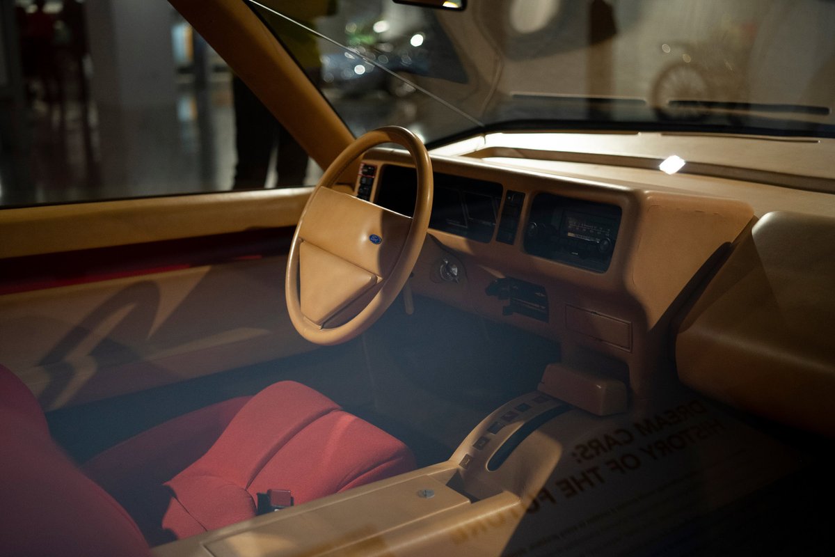 Ford 80s interior: Tan dash, steering wheel, and door trim contrast with bright red seats. Clear view of retro instrument cluster.