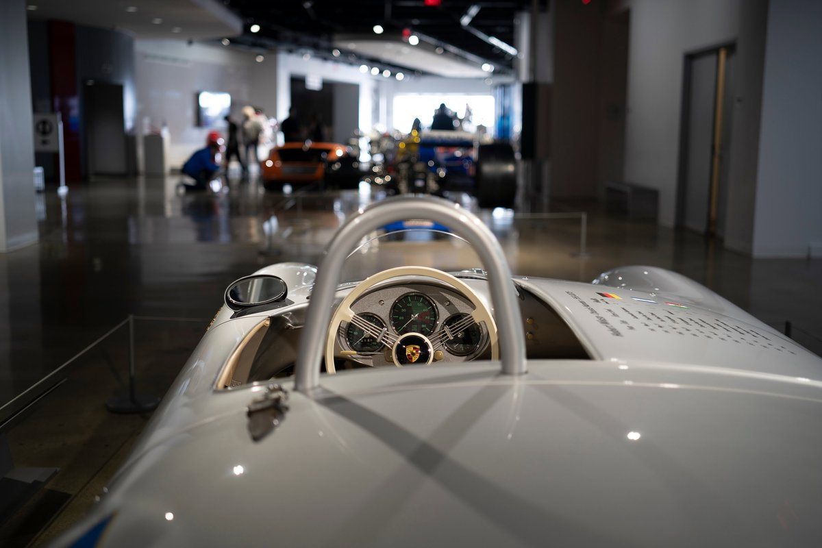 Silver Porsche 550 Spyder vintage race car cockpit featuring ivory steering wheel, analog gauges, and external rearview mirror.