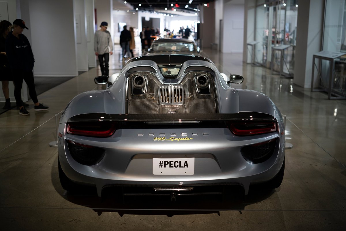 Metallic silver Porsche 918 Spyder rear view, featuring top-exit exhausts, carbon fiber trim, and gold badging. At PECLA.