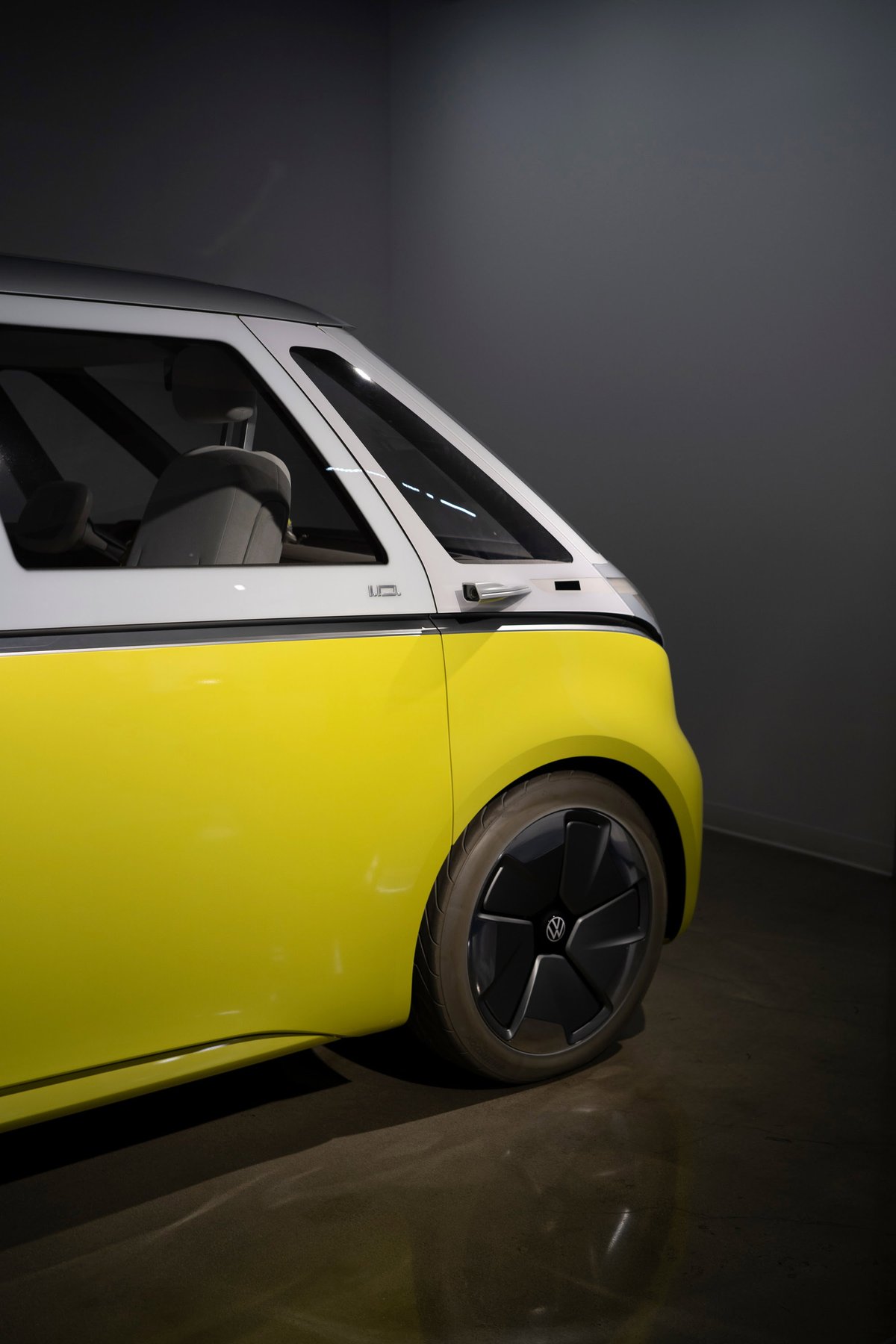 Front quarter view of a Volkswagen ID. Buzz in yellow and white two-tone livery, featuring black multi-spoke aero rims and silver body trim.