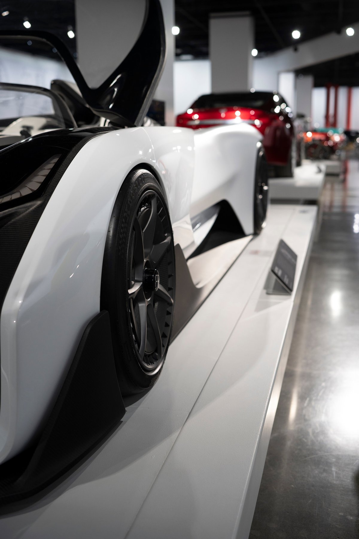 White Czinger 21C hypercar on display with open dihedral doors, showcasing carbon fiber aero trim and black multi-spoke rims.