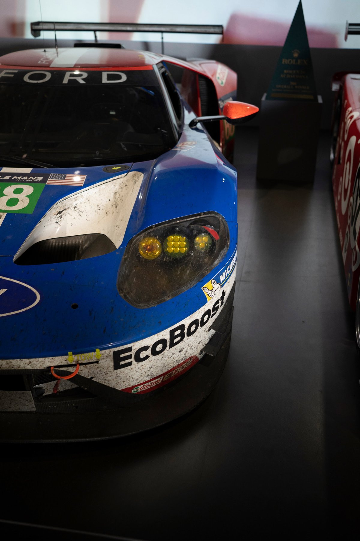 Front view of the dirty Ford GT GTE #68 Le Mans race car. Blue/white EcoBoost livery, prominent LED headlights, race grime.