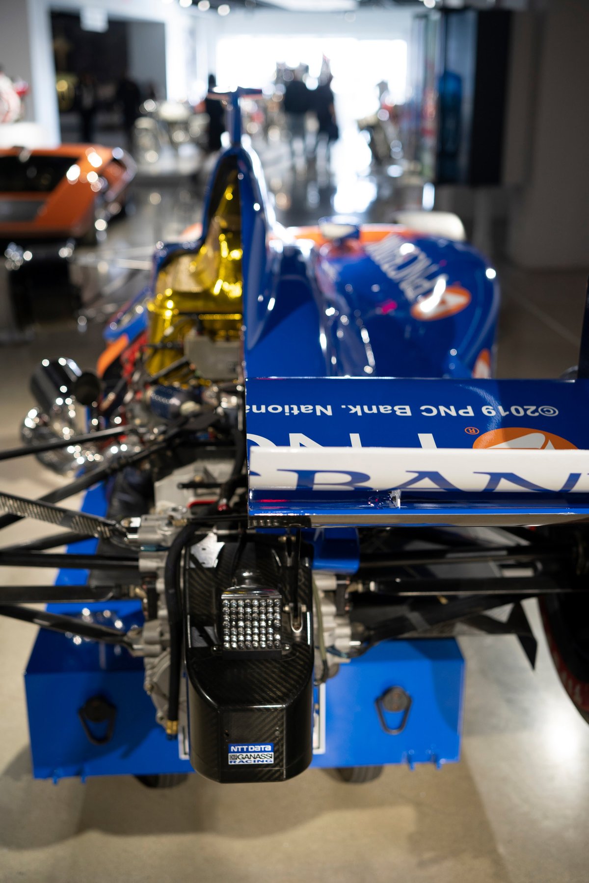 Rear view of a blue NTT DATA Ganassi Racing IndyCar, highlighting carbon fiber aero, gold engine detail, and sponsor livery.