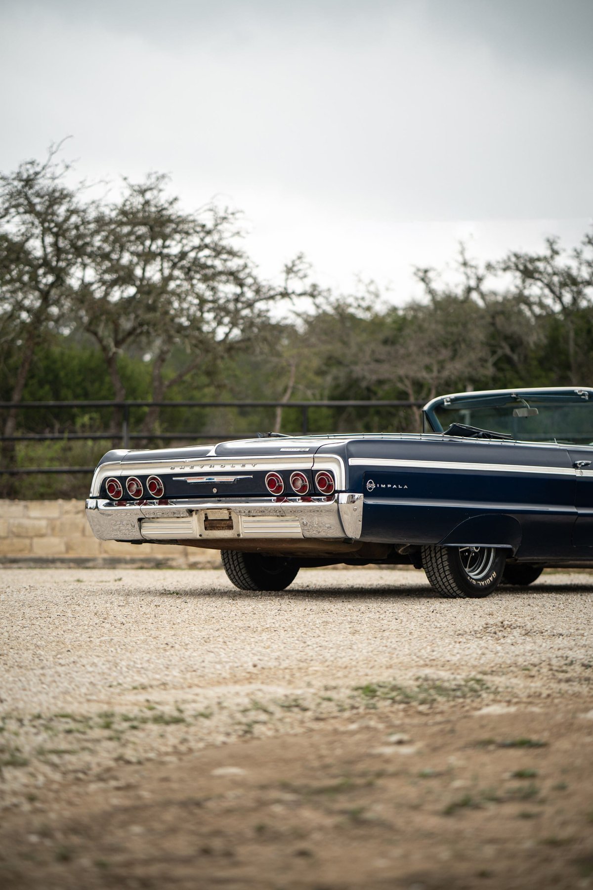 Rear view of a dark blue 1964 Chevrolet Impala SS convertible with chrome trim and quad taillights.