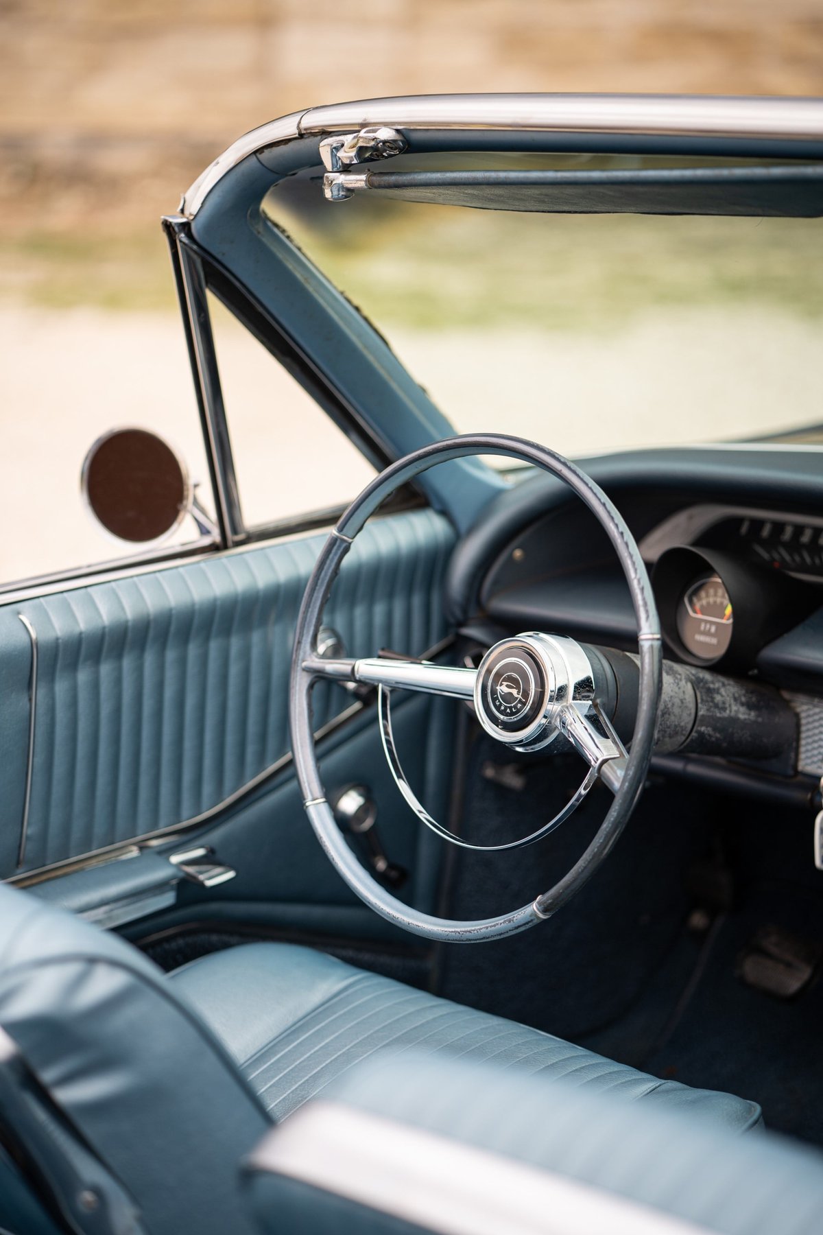 Interior of a 1964 Chevrolet Impala SS convertible, blue vinyl seats, dashboard and steering wheel.
