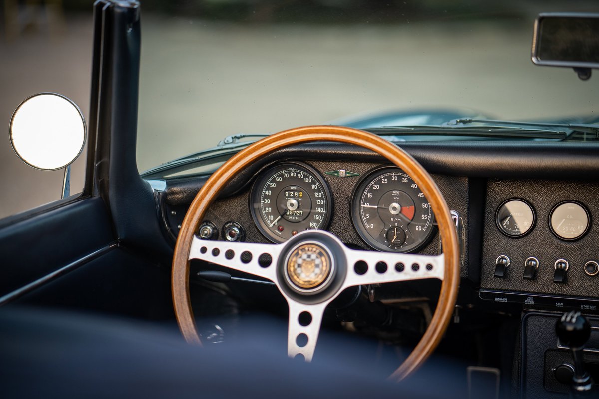 1966 Jaguar E-Type interior: wood-rimmed steering wheel, classic gauges, center console, and door trim.