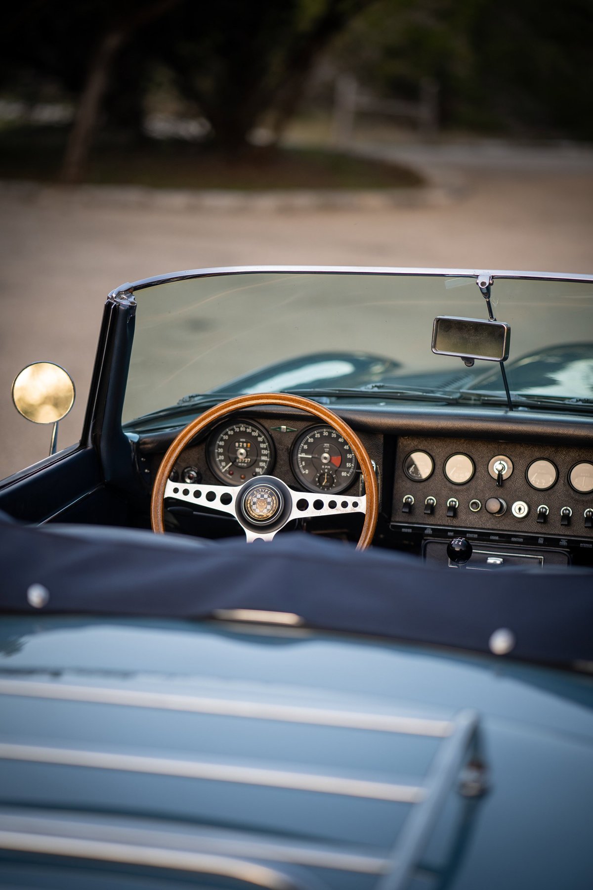 Close-up of a classic 1966 Jaguar XKE dashboard with wood steering wheel and opalescent silver-blue exterior trim.