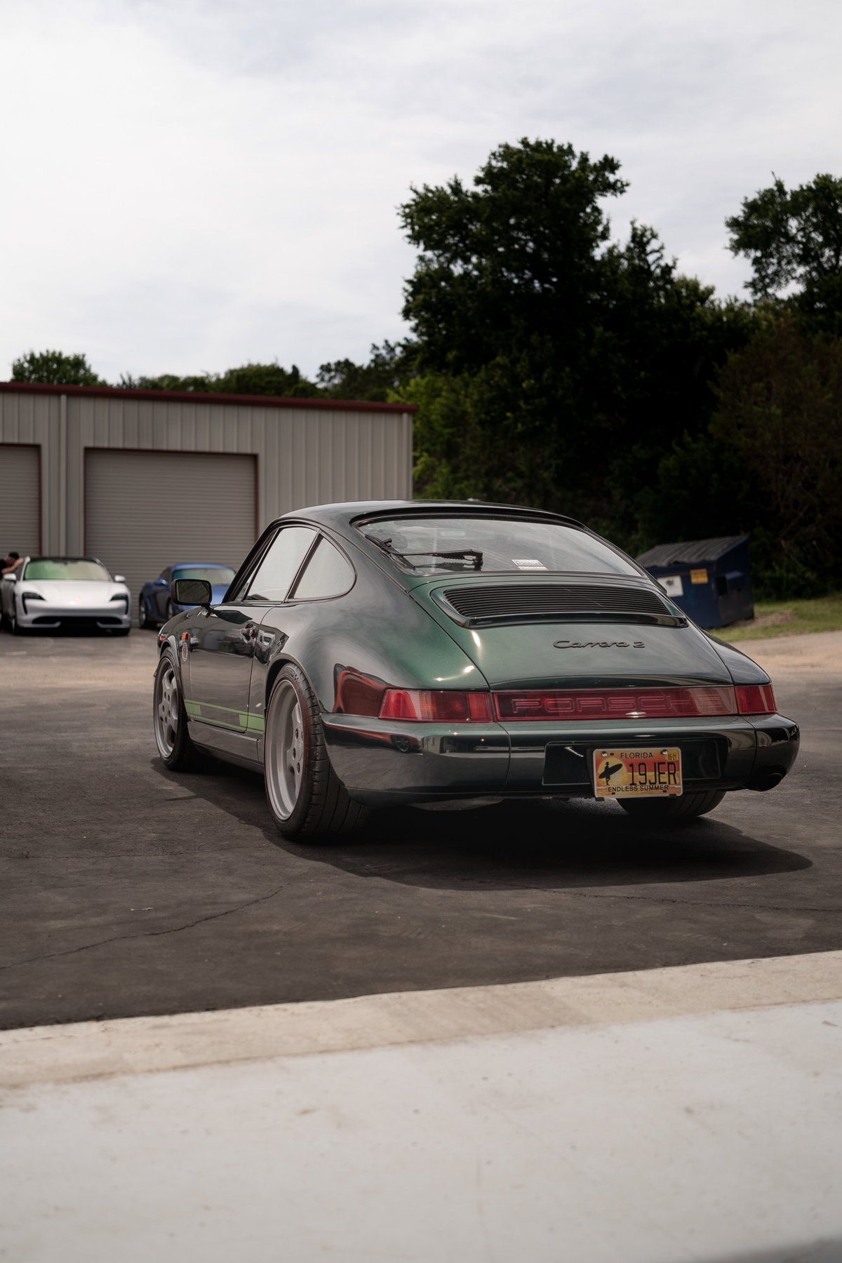 The rear of a dark green Porsche 911 Carrera 2, with silver rims and a green stripe.