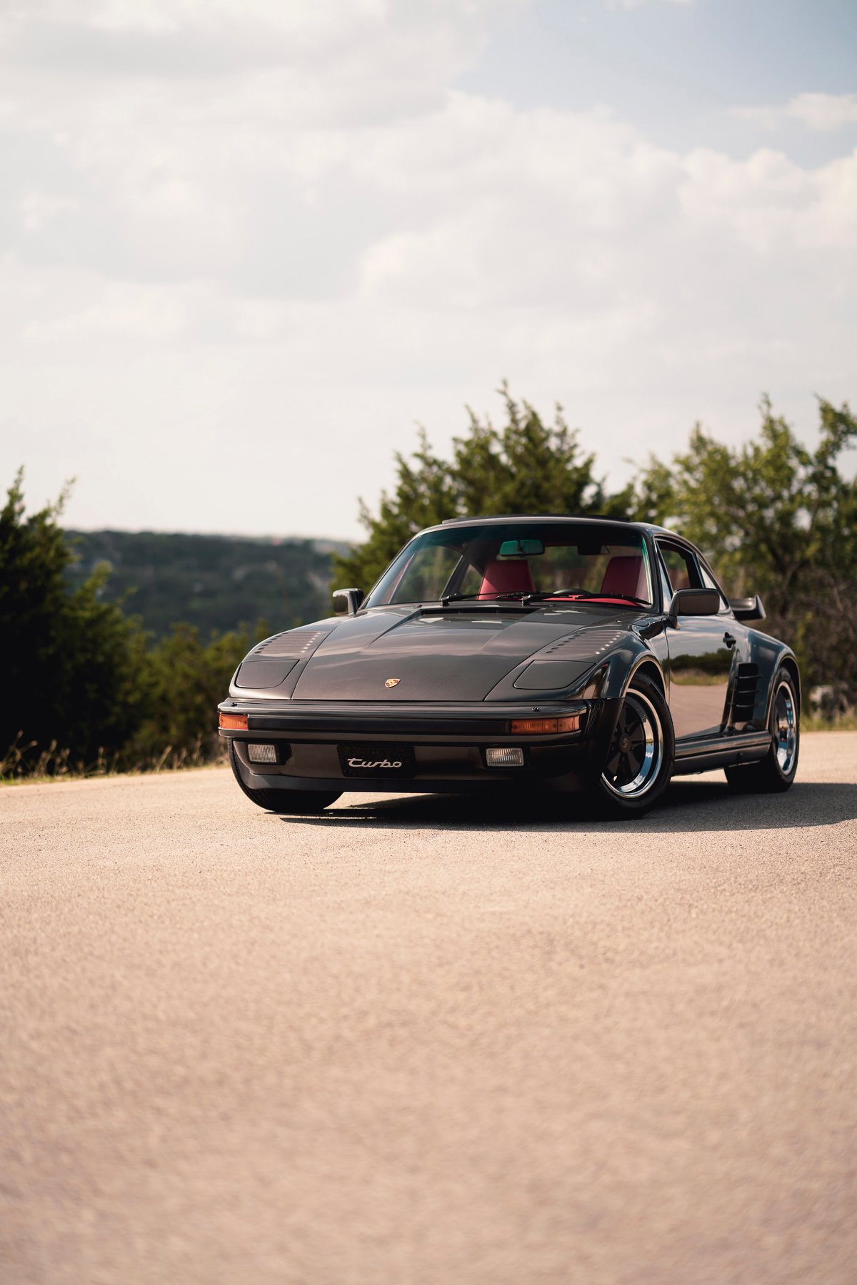 1989 Porsche 930 Turbo Flachbau in dark grey with red interior and distinctive front fender trim.