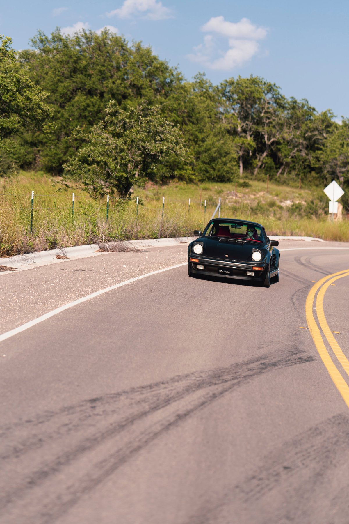 Black 1989 Porsche 930 Turbo Flachbau with red interior on a winding road.