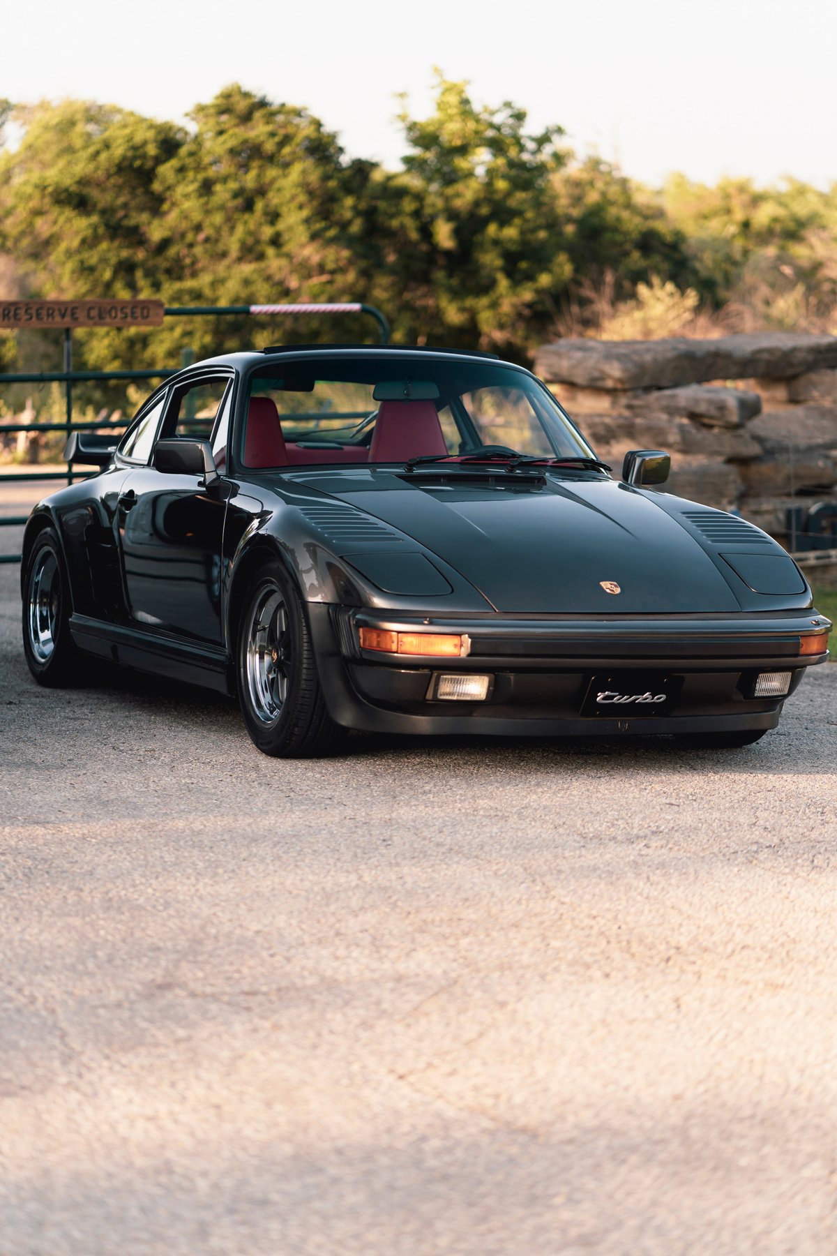 Dark grey 1989 Porsche 930 Turbo Flachbau with red interior and gold BBS rims.