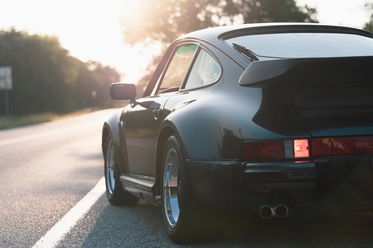 1989 Porsche 930 Turbo Flachbau rear-quarter view, black exterior with classic turbo spoiler and alloy rims.
