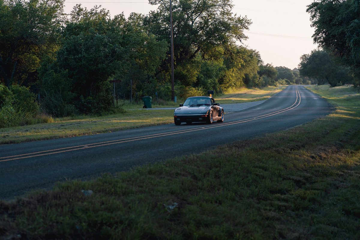 Black 1989 Porsche 930 Turbo Flachbau convertible on a country road.