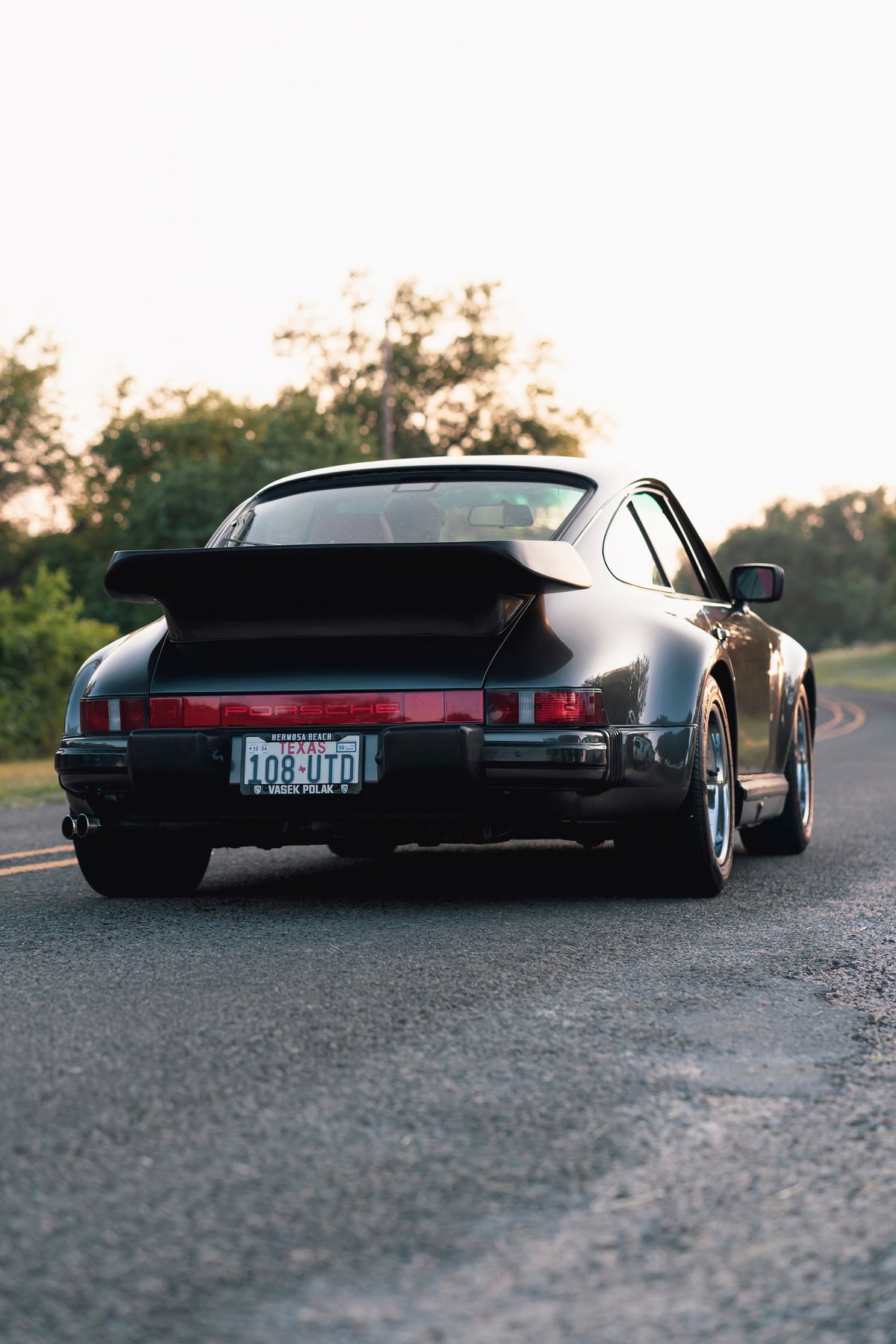 Rear view of a black 1989 Porsche 930 Turbo Flachbau with a whale tail spoiler and chrome rims.