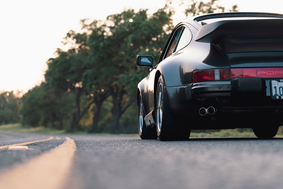 Rear view of a black 1989 Porsche 930 Turbo Flachbau with a whale tail spoiler and dual exhaust.