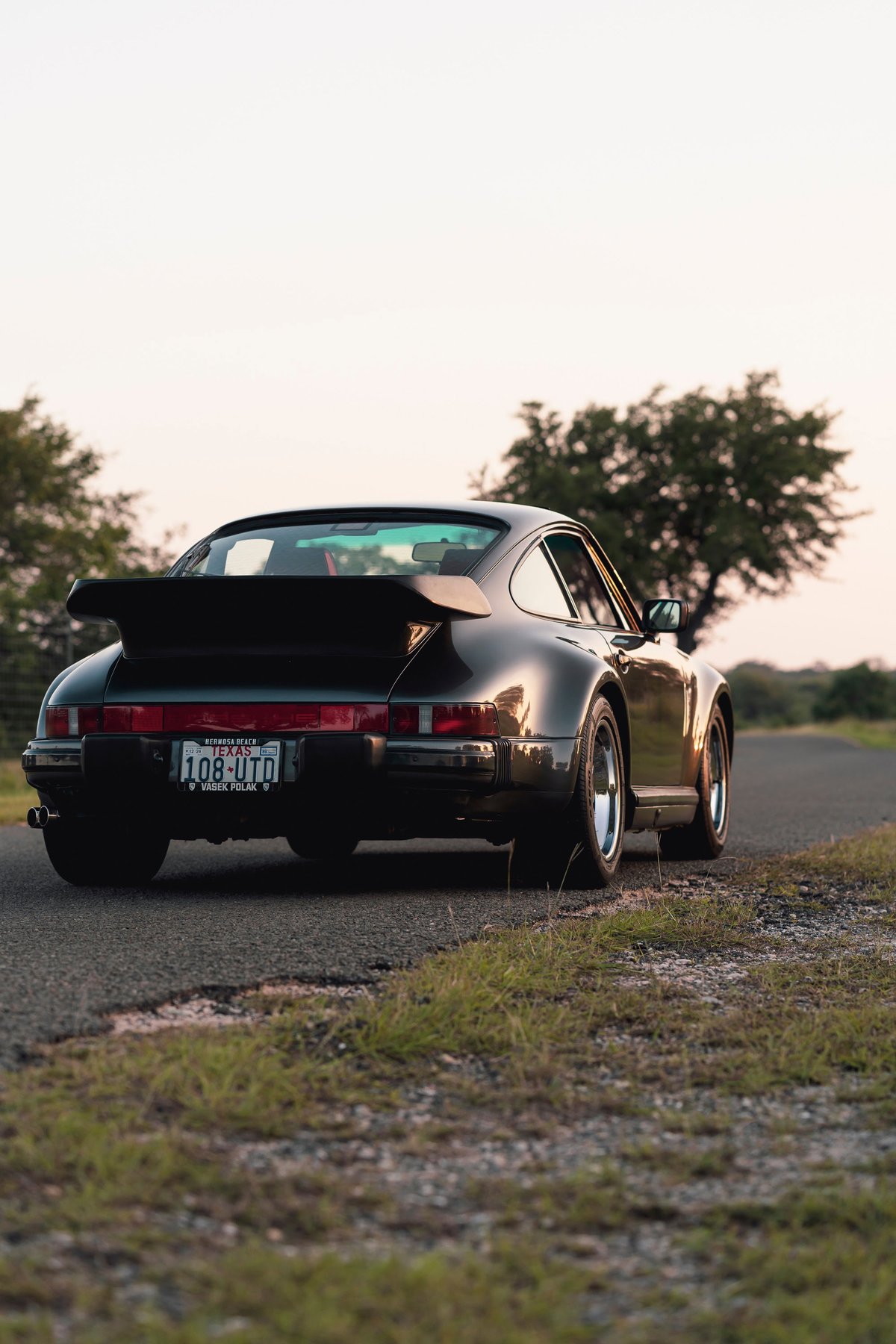 1989 black Porsche 930 Turbo Flachbau with a whale tail spoiler, chrome rims.
