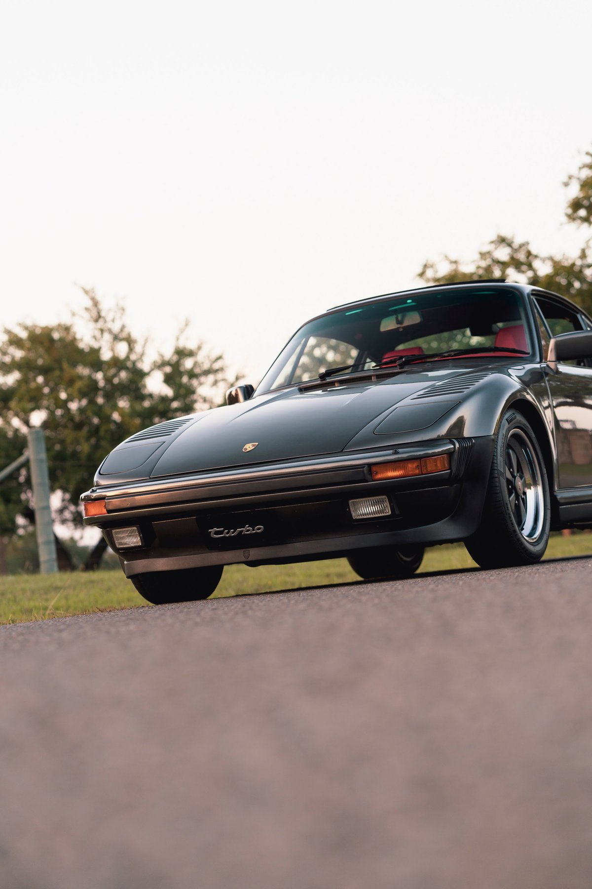 Black 1989 Porsche 930 Turbo Flachbau with red interior, chrome trim, and black rims.