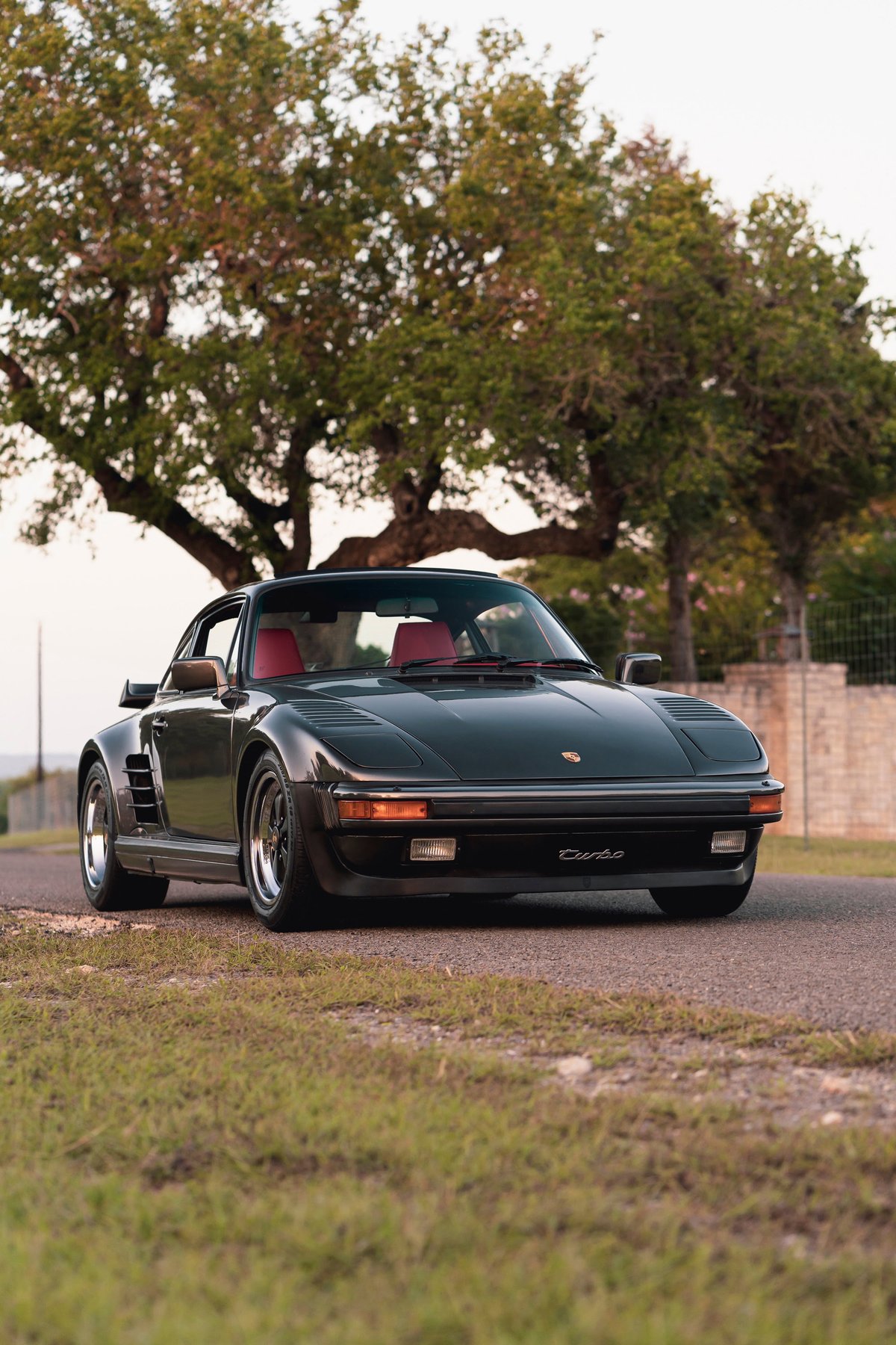 A dark grey 1989 Porsche 930 Turbo Flachbau with red interior and chrome rims.