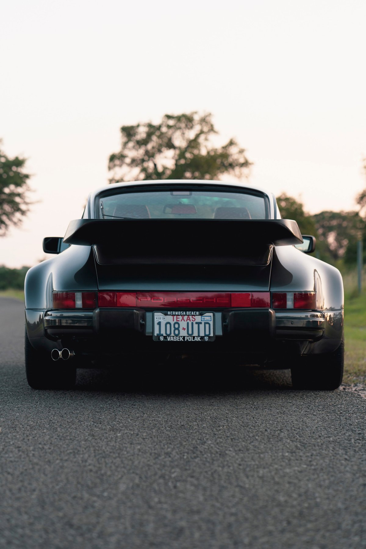 Black 1989 Porsche 930 Turbo Flachbau rear view with whale tail spoiler and dual exhaust.