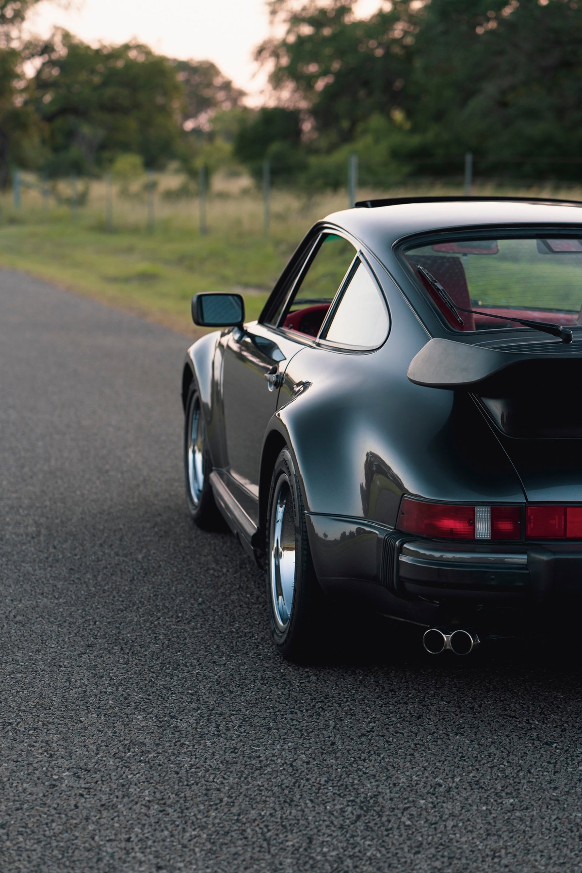 Rear view of a black 1989 Porsche 930 Turbo Flachbau with chrome rims and dual exhaust.