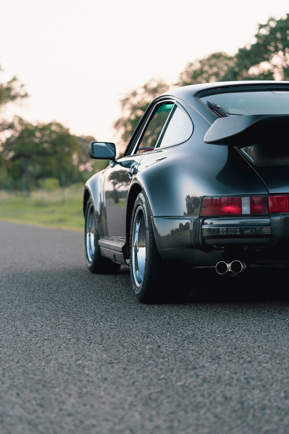 1989 Porsche 930 Turbo Flachbau in black, with chrome rims and twin exhaust.