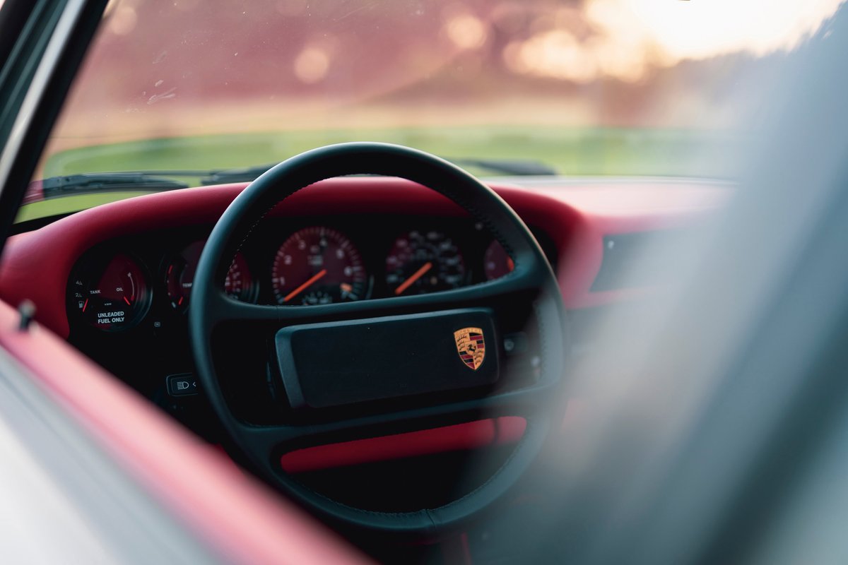 1989 Porsche 930 Turbo Flachbau interior with red trim and Porsche crest on steering wheel.