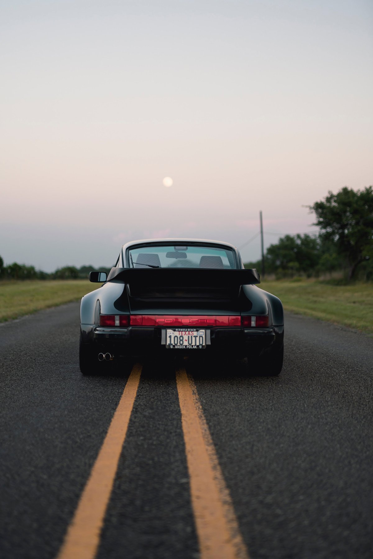 Black 1989 Porsche 930 Turbo Flachbau with whale tail spoiler on a lonely road.