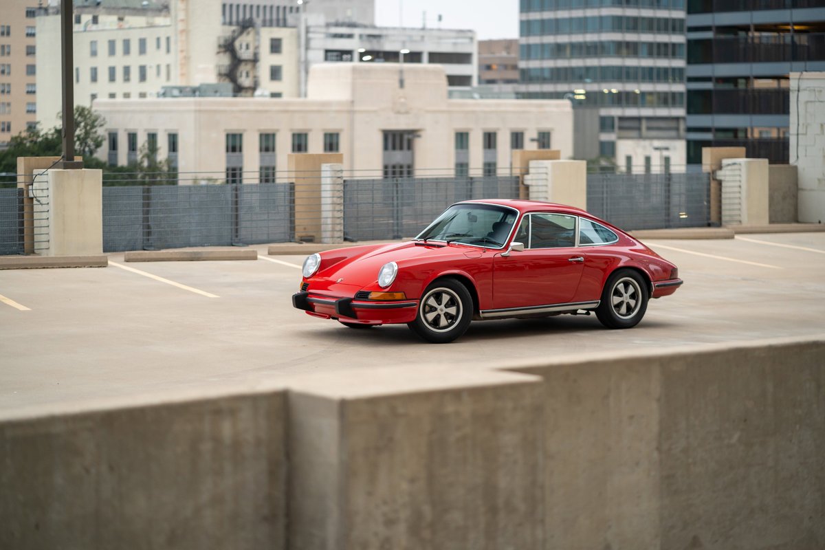 A red 1973 Porsche 911S coupe with classic Fuchs rims parked on a rooftop.