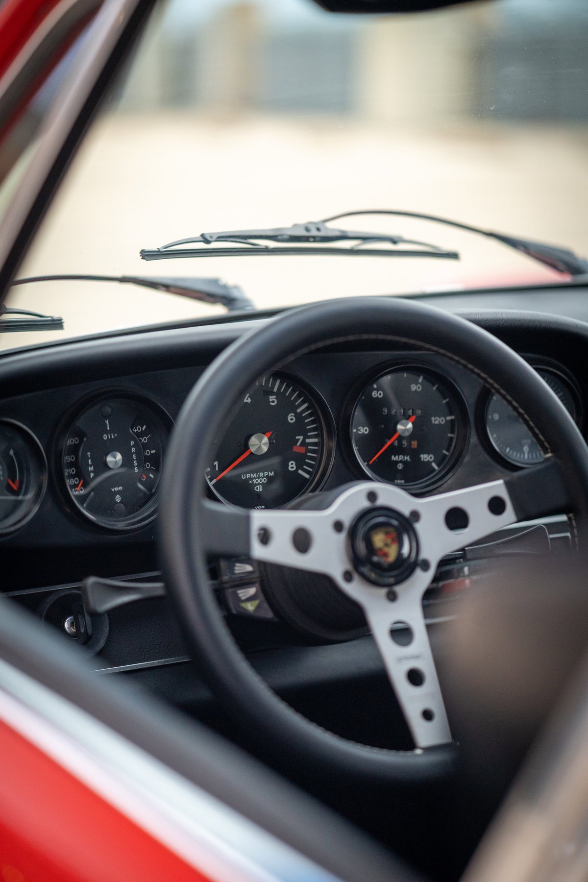 Interior of a red 1973 Porsche 911S showing a classic steering wheel and instrument cluster.