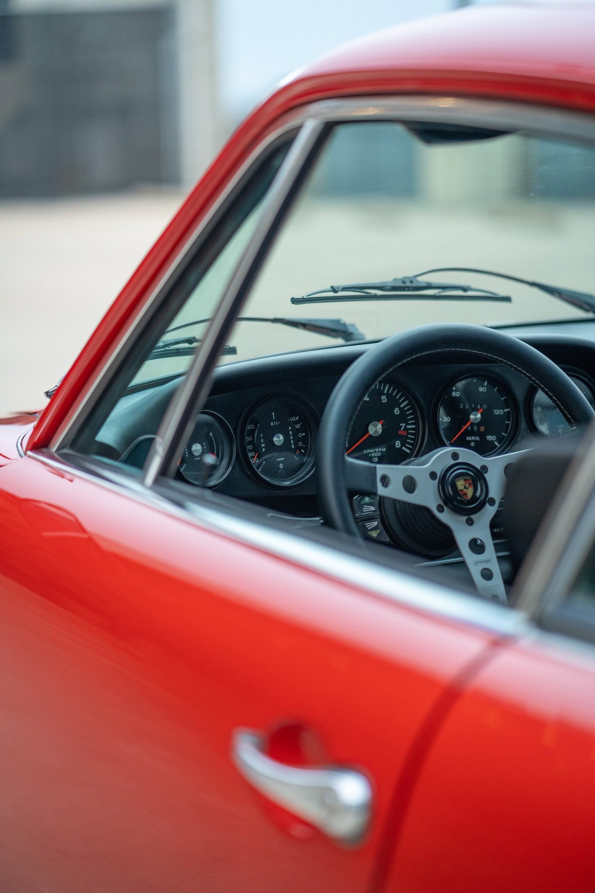 Close-up interior shot of a red 1973 Porsche 911S, showing the classic dashboard and steering wheel.