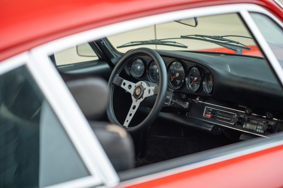 Interior shot of a 1973 Porsche 911S, featuring a vintage steering wheel and classic dashboard gauges.