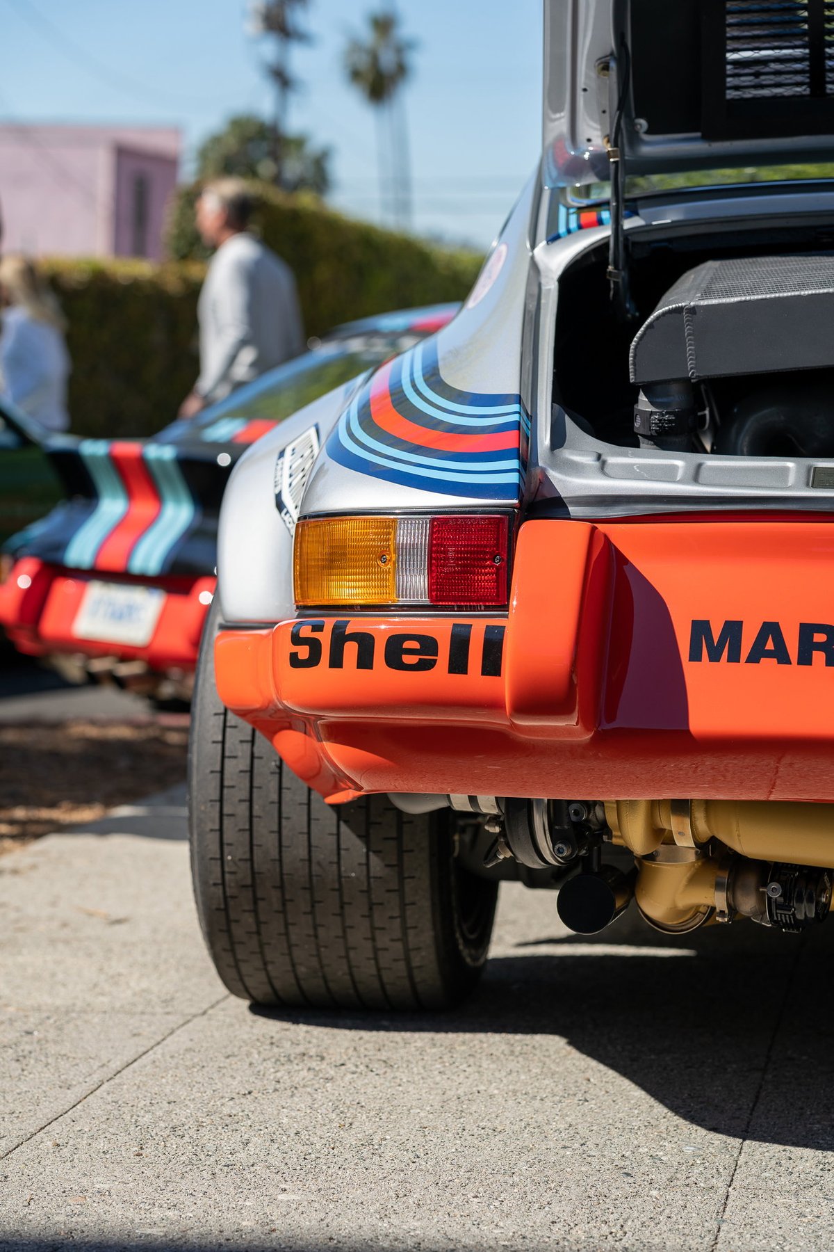 Close-up rear view of a silver Porsche 911 with Martini Racing livery, orange trim, and "Shell" branding.