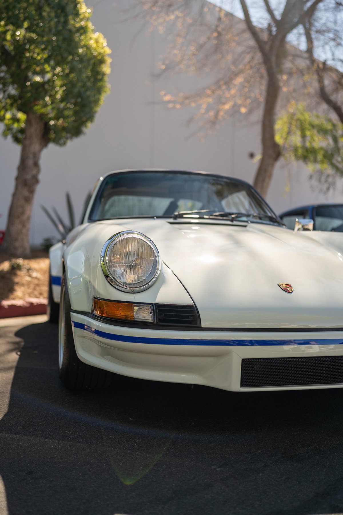 White classic Porsche 911 with blue livery trim and chrome rims.