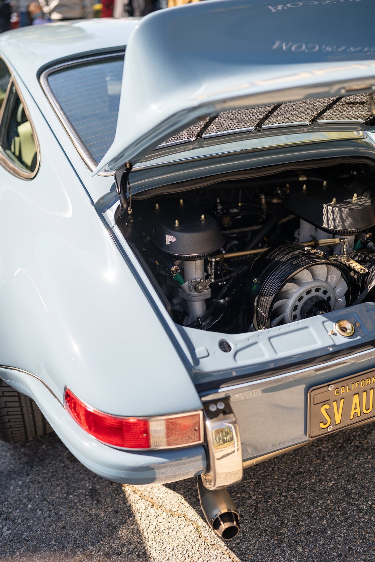 Light blue 1973 Porsche 911 T with exposed flat-six engine, chrome trim, and California plate.