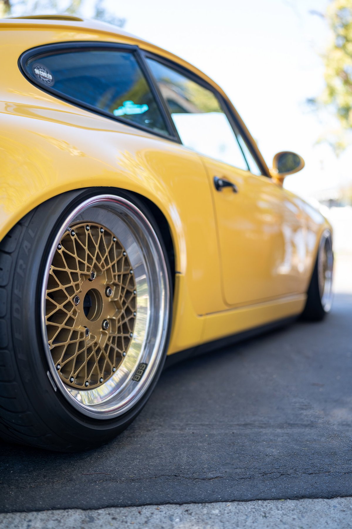 Low profile yellow Porsche 911 with gold mesh BBS rims and slammed suspension.