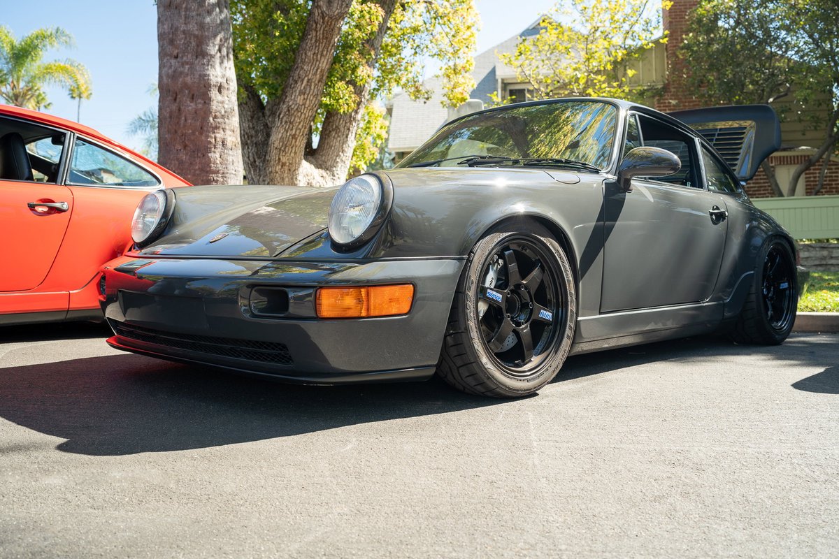 A gray Porsche 911 with aftermarket black rims and a ducktail spoiler.